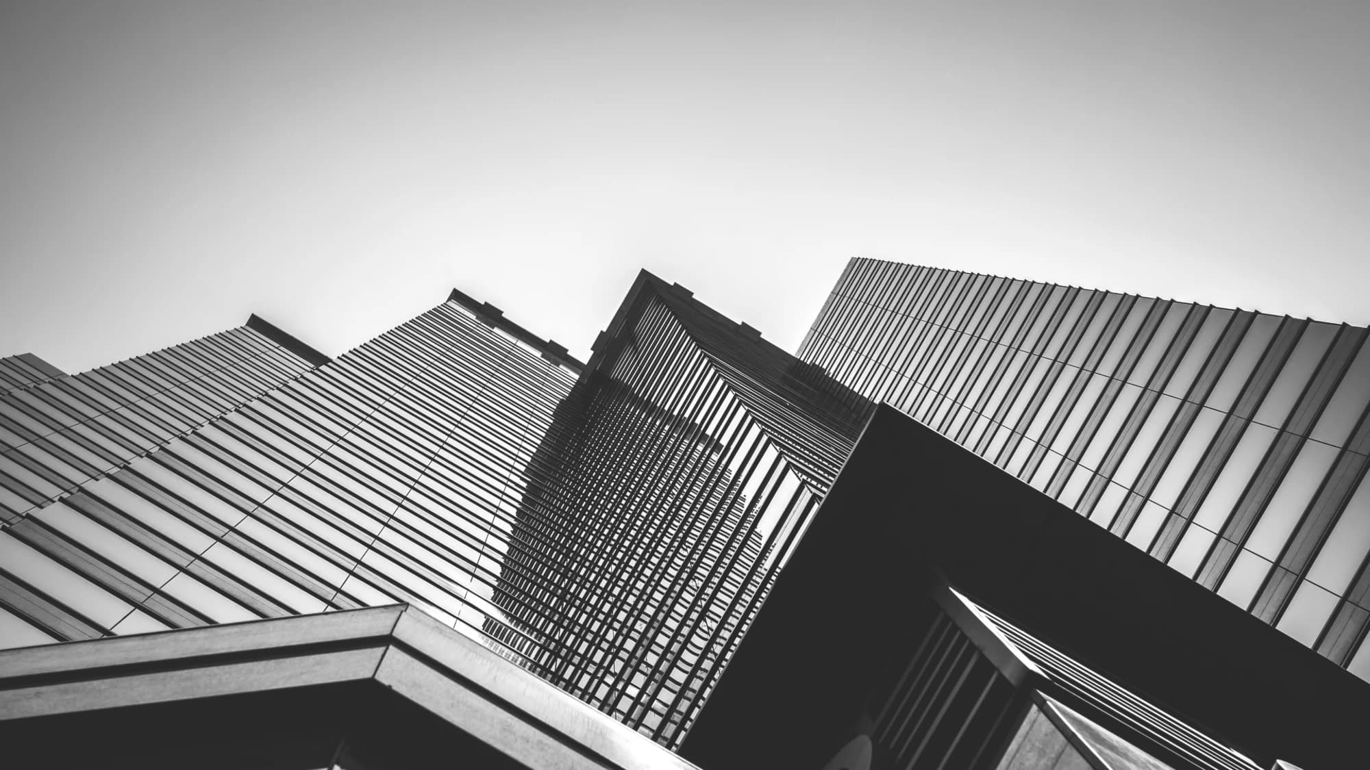 Upward view of angular financial-district towers against a pale sky, monochrome