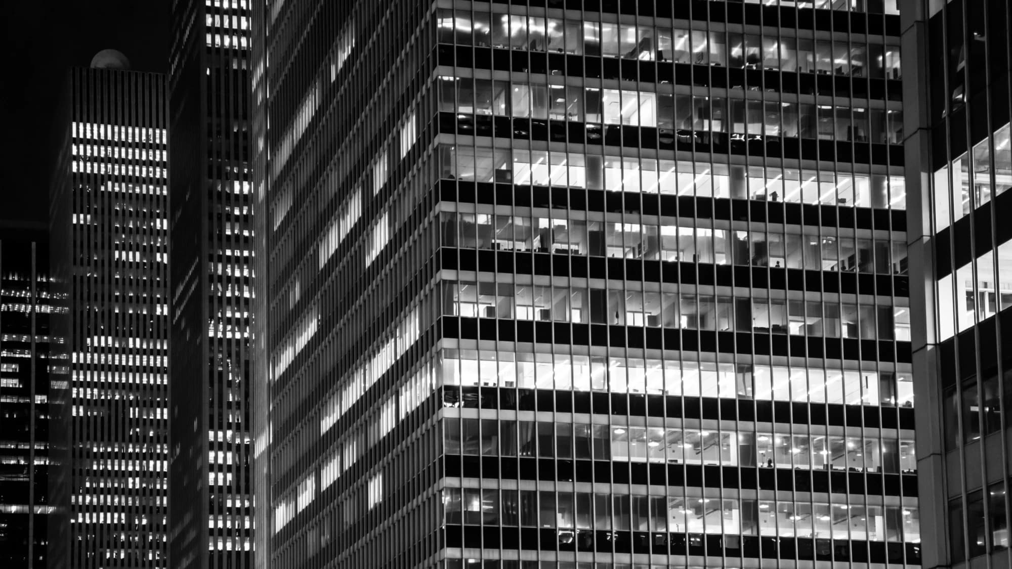 Illuminated office floors of a commercial tower at night, monochrome