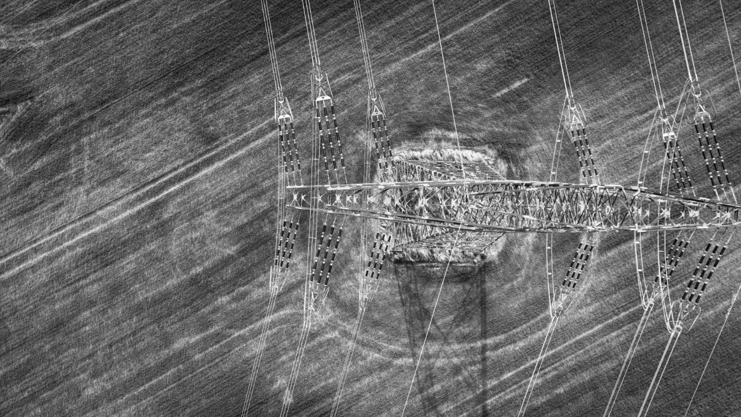 Aerial view of a high-voltage transmission tower with power lines radiating across a plowed field, monochrome